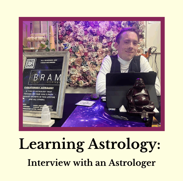 Astrologer, Brandon Ramsey, smiling at a table with a sign about evolutionary astrology